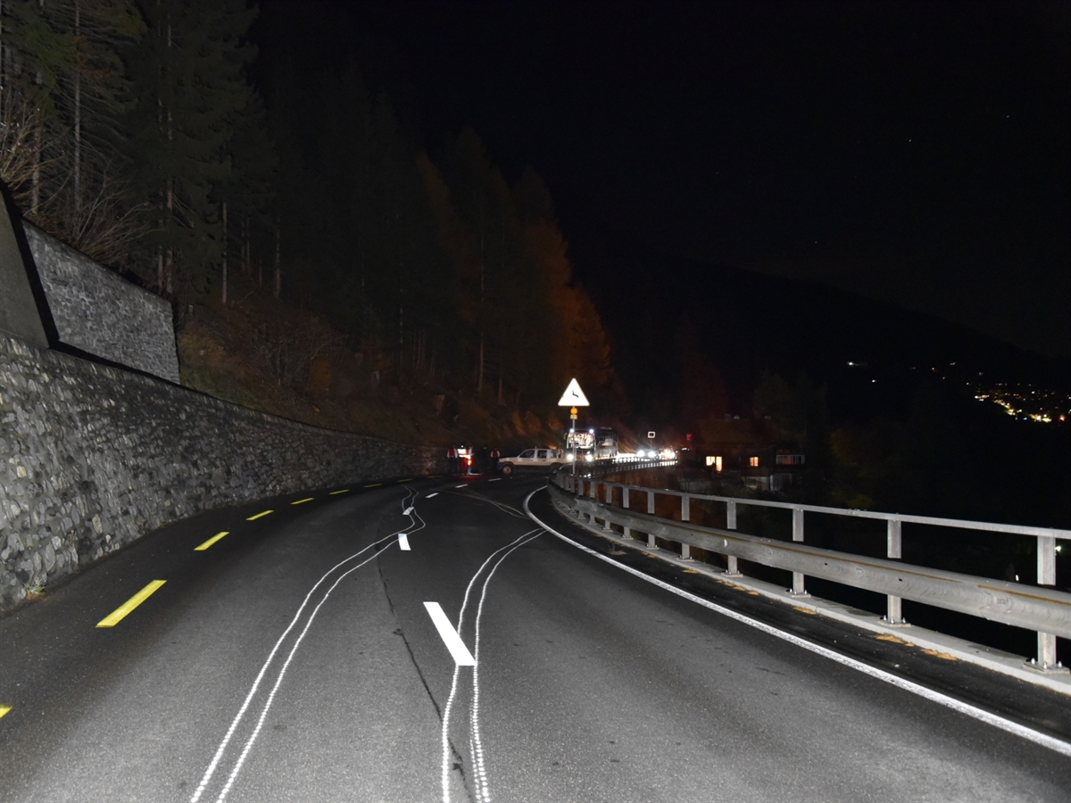 Weiss angezeichnete Schleuderspuren, die nach rechts zur Leitplanke und nach links zur Stützmauer verlaufen. Im Hintergrund quer auf der Strasse das verunfallte Auto.