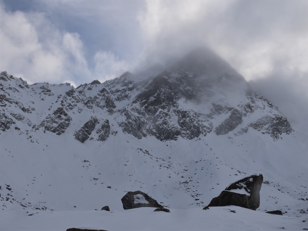 Blick von unten auf den Piz Radönt und die Nordostrinne. Die Landschaft ist mit Schnee bedeckt. Bewölkung und blauer Himmel grenzen den Horizont ab.
