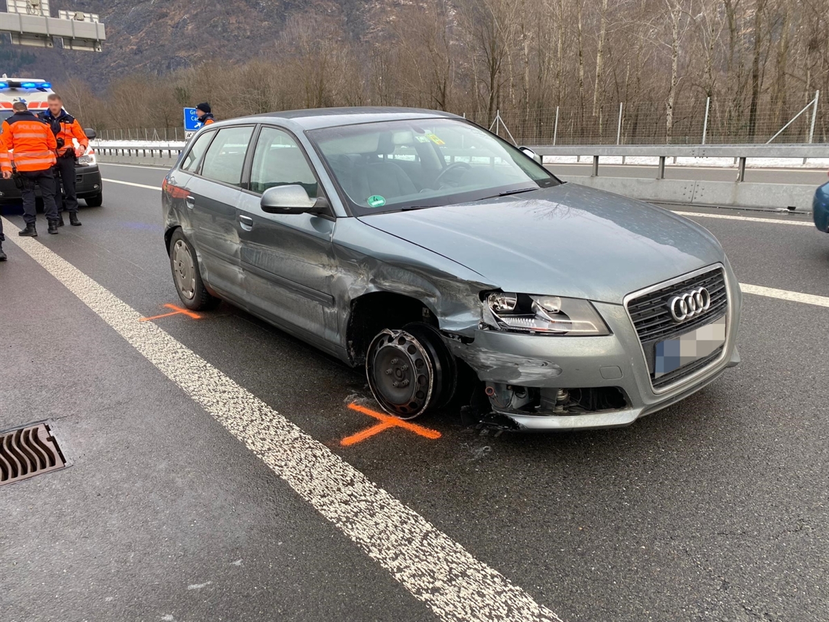 Das beschädigte Unfallfahrzeug auf der Autobahn A13. Im Hintergrund ein Ambulanzfahrzeug und davor drei Polizisten.