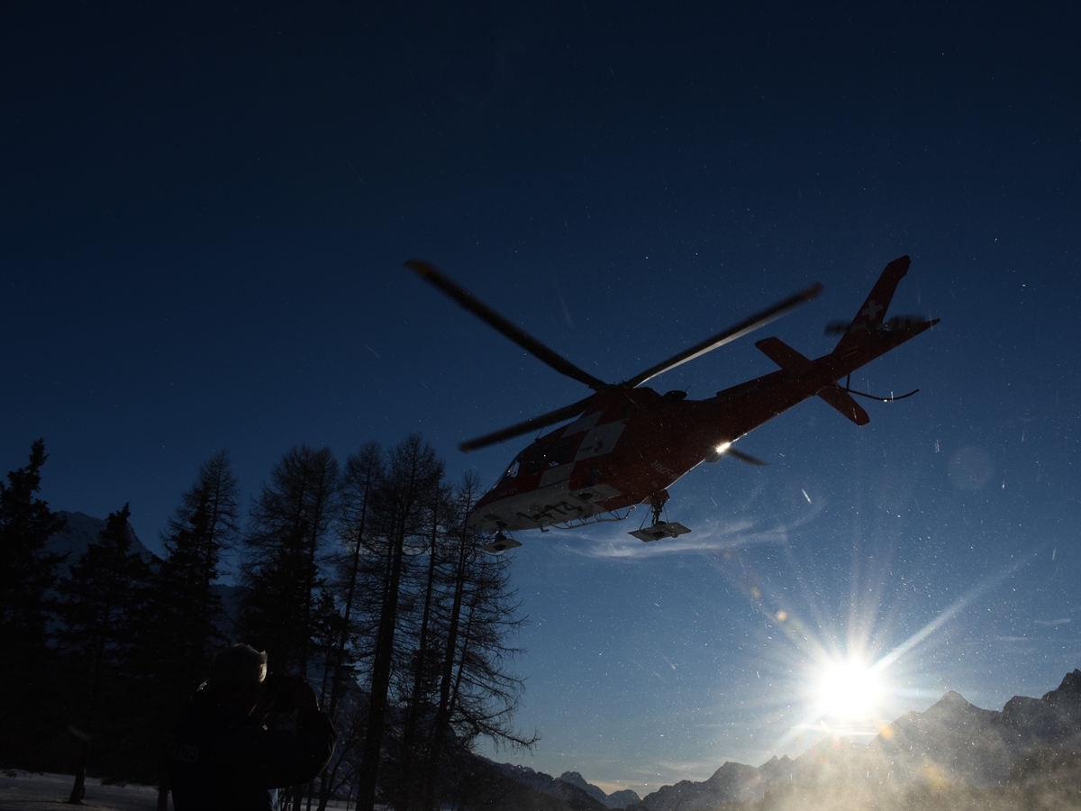 Der Rega-Helikopter in der Luft. Im Hintergrund Berge und Winterstimmung.