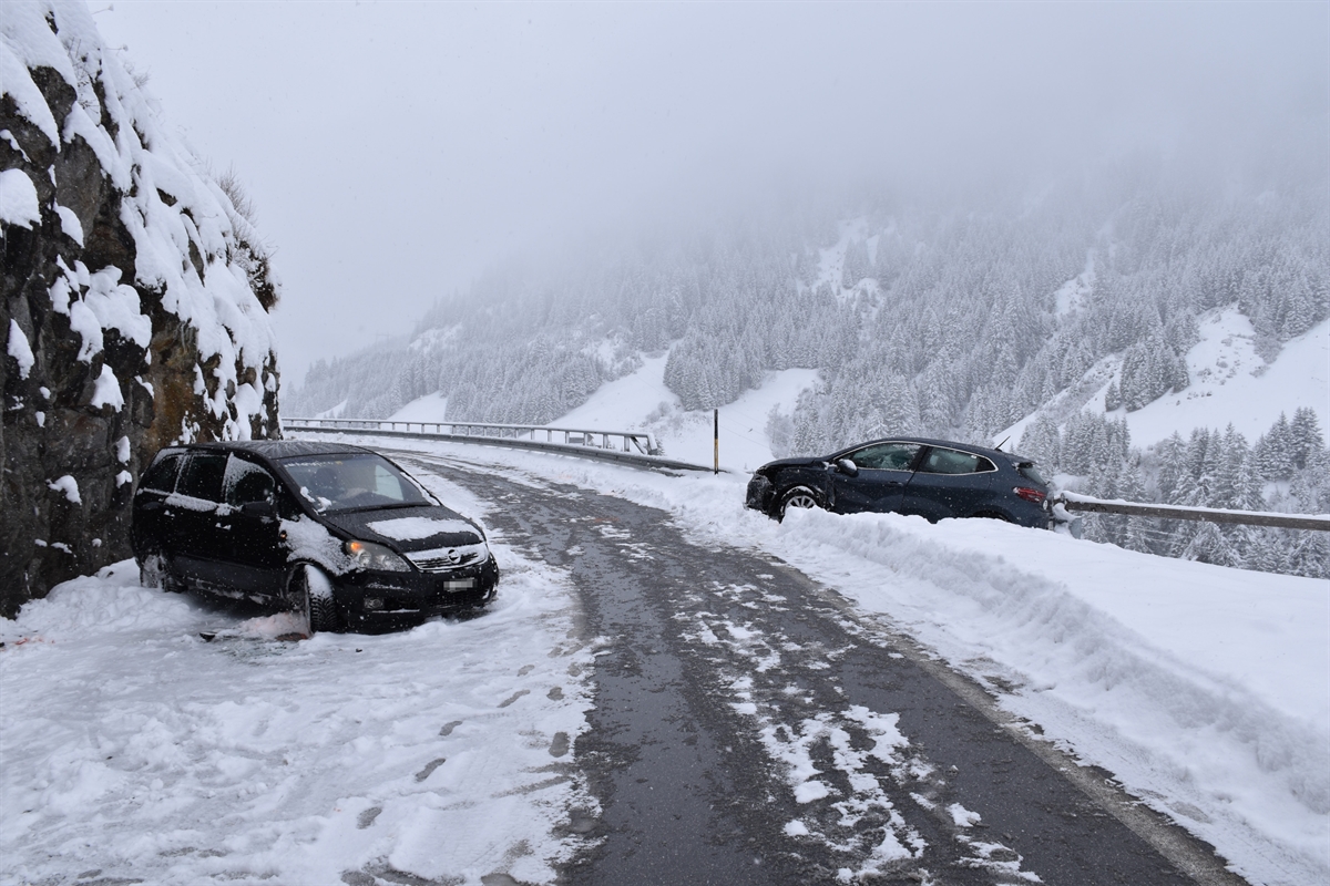 Strassenverlauf der zum Teil schneebedeckten Lukmanierstrasse im Bereich der Unfallstelle, Höhe Platta, in Fahrtrichtung Passhöhe gesehen. Auf der linken Seite ist ein unfallbeteiligtes Fahrzeug zu erkennen. Auf der rechten Seite das andere beteiligte Fahrzeug in der Endlage am Bündnerzaun anliegend.