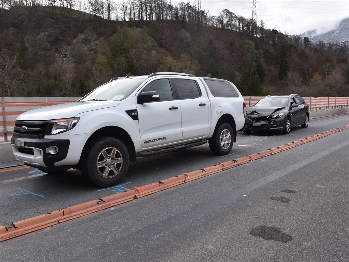 Rechts im Bild der weisse Lieferwagen und dahinter das dunkle Auto. Die Front des Autos ist stark beschädigt. Beide Fahrzeuge stehen im Baustellenbereich.