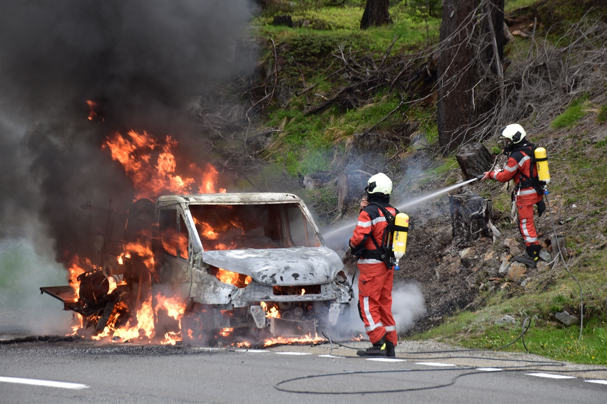 Zwei Feuerwehrleute spritzen Wasser auf den brennenden Lieferwagen