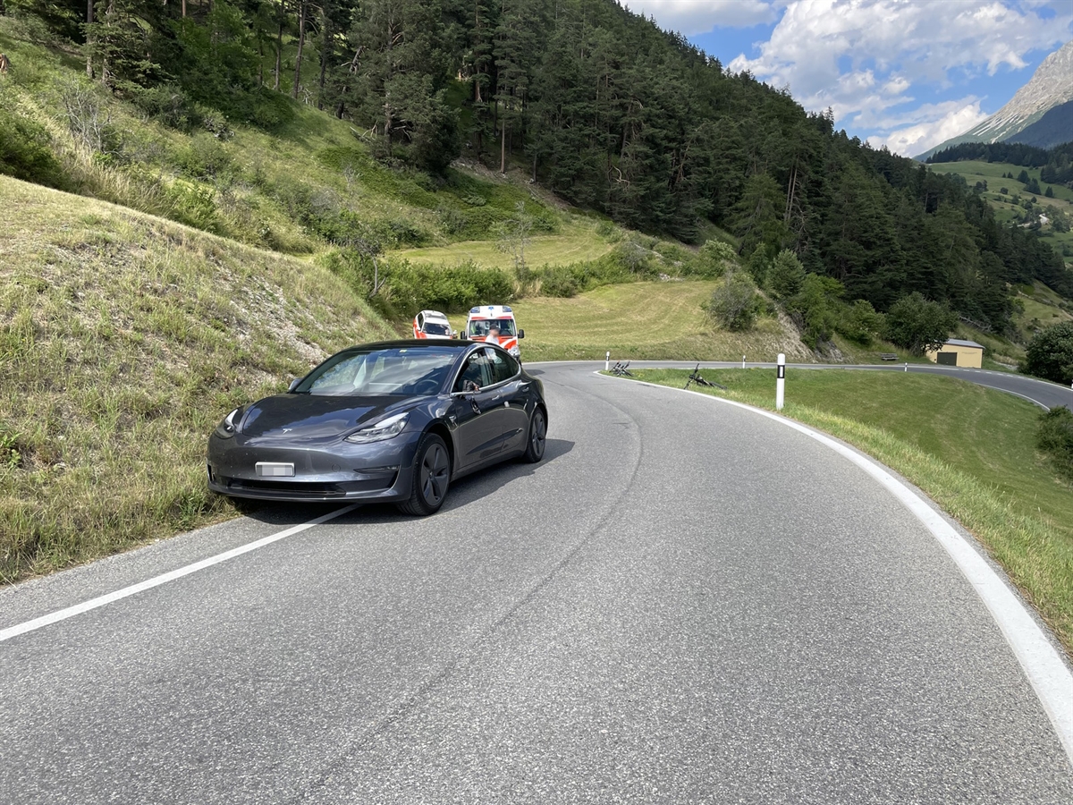 Die Strasse beschreibt eine Links- und anschliessend eine starke Rechtskurve. Links das Unfallauto, dahinter Einsatzfahrzeug. Rechts an der Strasse zwei Fahrräder.