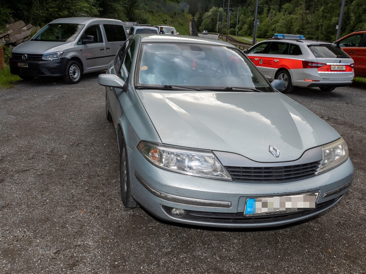 Im Vordergrund das silberne Auto der drei. Im Hintergrund weitere Fahrzeuge, darunter ein Polizeiauto.