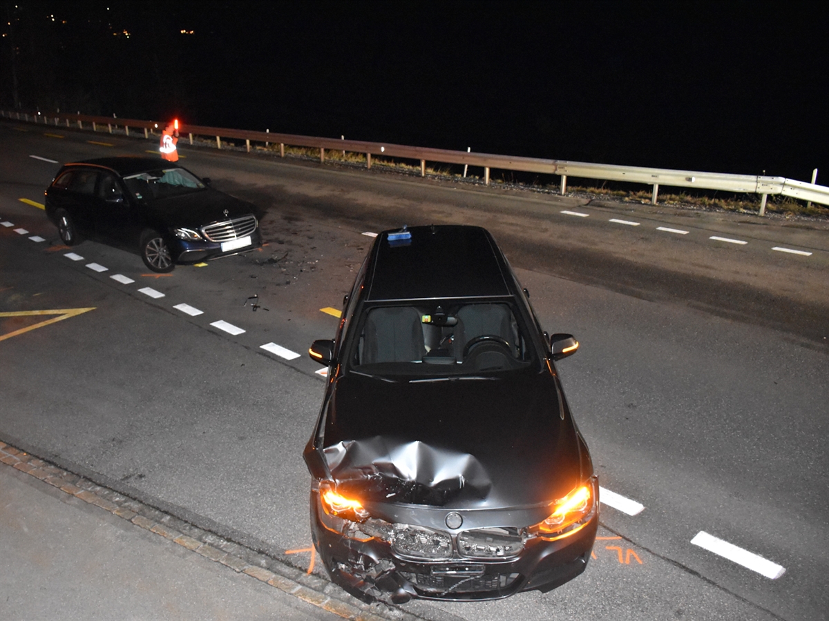 Ein Polizist lenkt den Fahrzeugverkehr auf der Oberalpstrasse bei Trin mit Hilfe einer Stablampe an den beiden Unfallfahrzeugen vorbei