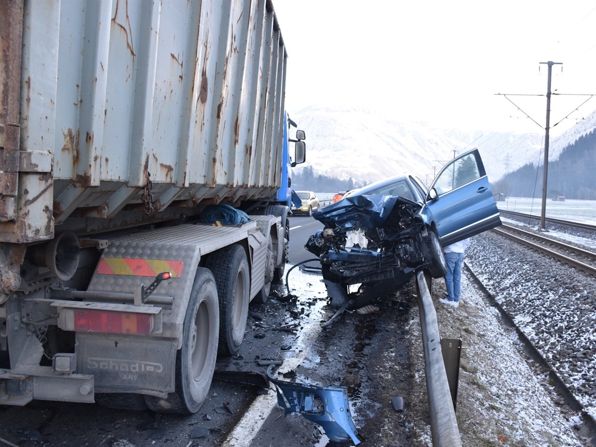 Auf der linken Bildseite ist die Fahrzeugseite des Lastwagens erkennbar. Rechts davon ist das Auto auf der Leitplanke.