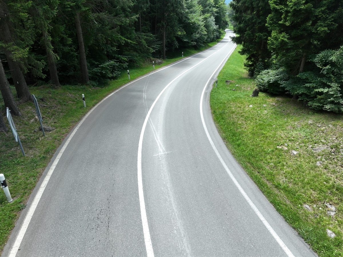 Drohnenbild der Rechtskurve der Luzisteigstrasse. In dieser Rechtskurve sind Bremsspuren über die Fahrbahn eingezeichnet. Links und rechts wird die Strasse von Wald begrenzt.