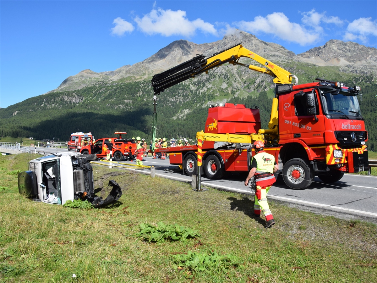 Der in einer Böschung auf der Seite liegende Kleinbus. Auf der Strasse ein Abschleppfahrzeug mit Kran sowie Einsatzkräfte.