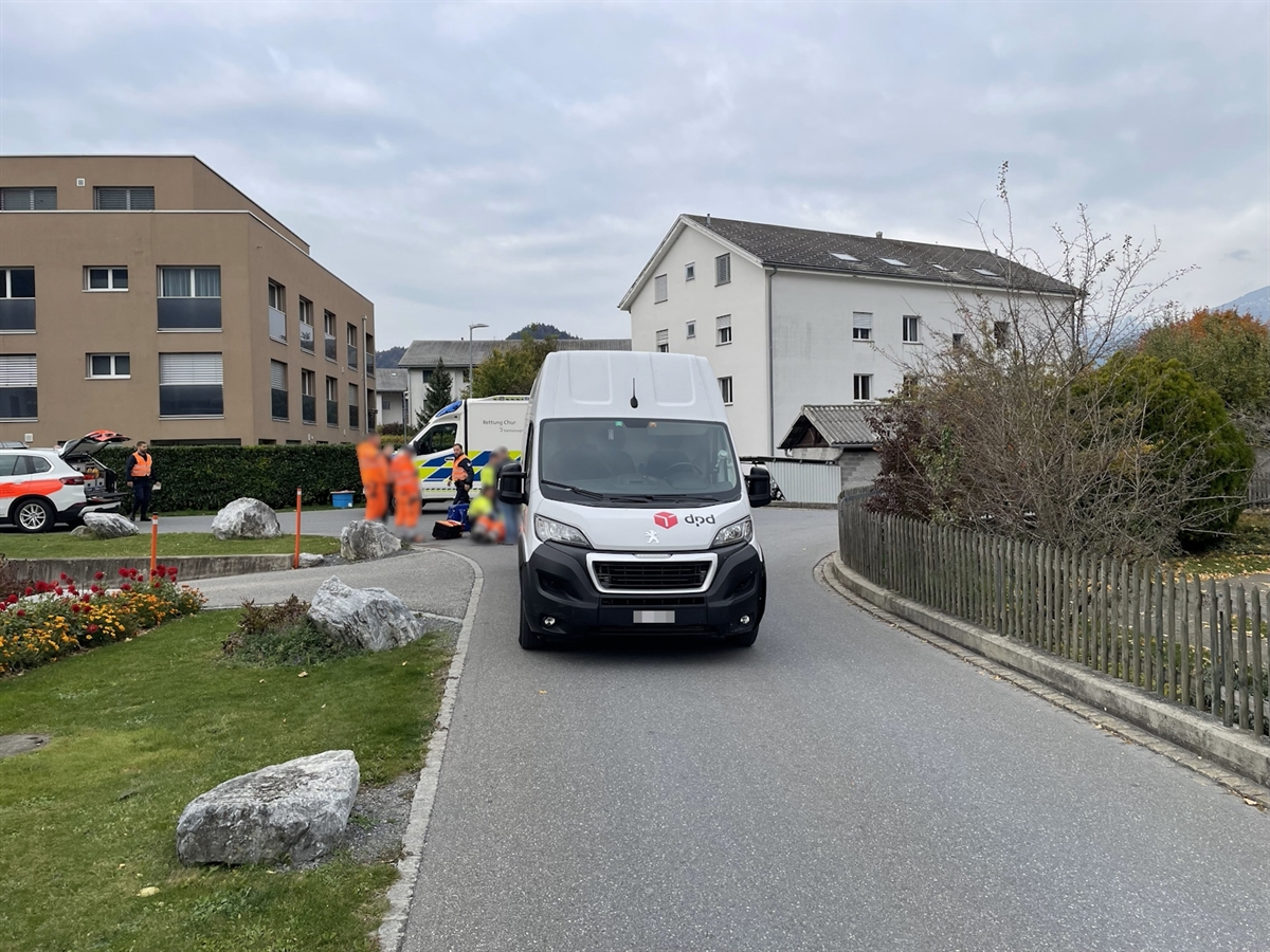 Der Lieferwagen auf der Via Ginellas. Hinter dem Fahrzeug betreut ein Rettungsteam den am Boden liegenden Verletzten. Arbeitskollegen und der Chauffeur sowie zwei Polizisten sind ebenfalls anwesend